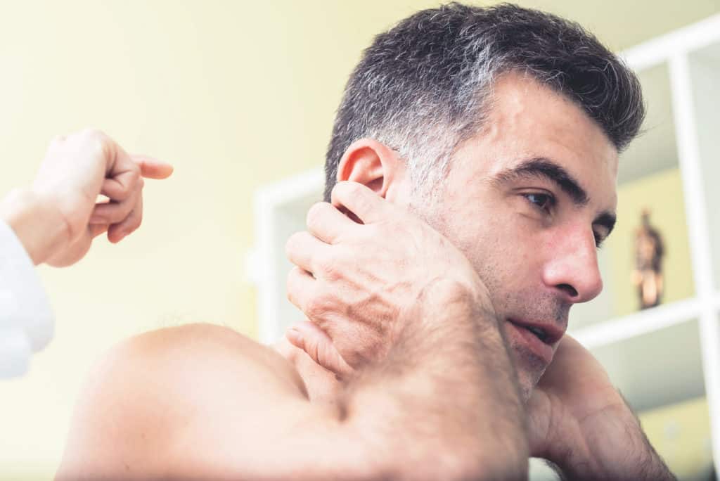 Male patient at the doctor's office shows a site of pain that will be treated with acupuncture. Optimistic facial expression