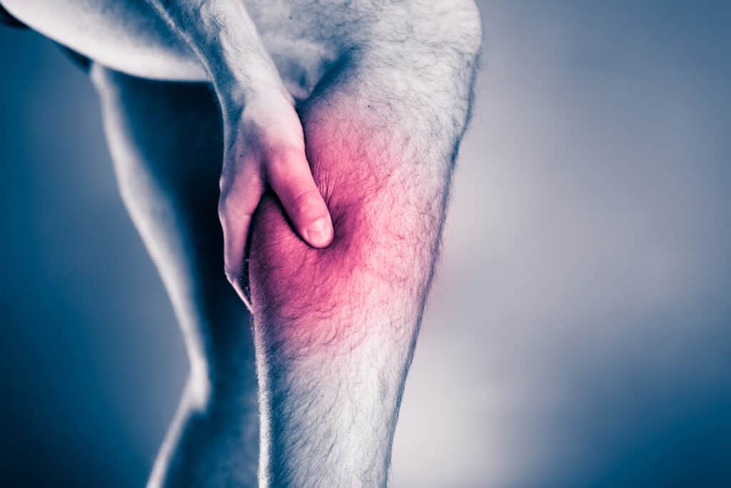 Calf pain, physical injury. Male leg and muscle pain from running or training, sport physical injuries when working out. Man athlete holding leg with painful red spot over black and white background.